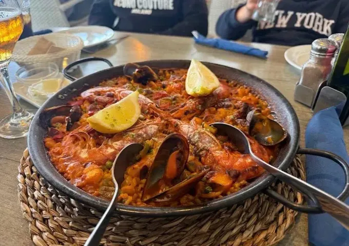 Paella de marisco en una sartén negra con rodajas de limón en la mesa de un restaurante.
