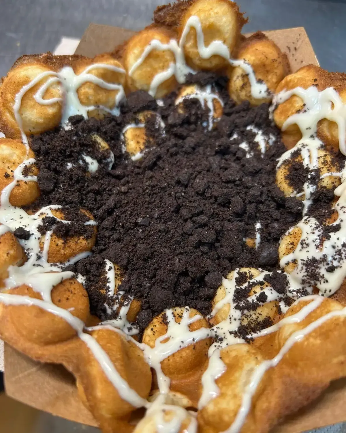 Postre de waffle de burbujas con migas de galletas y un chorrito de salsa blanca.