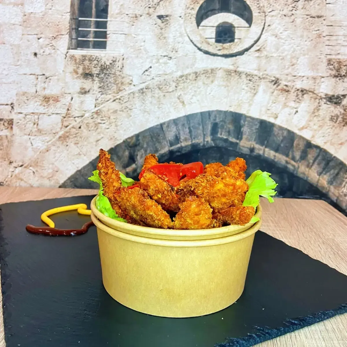 Nuggets de pollo frito en un recipiente de papel con salsa de tomate, lechuga y mostaza sobre una superficie negra