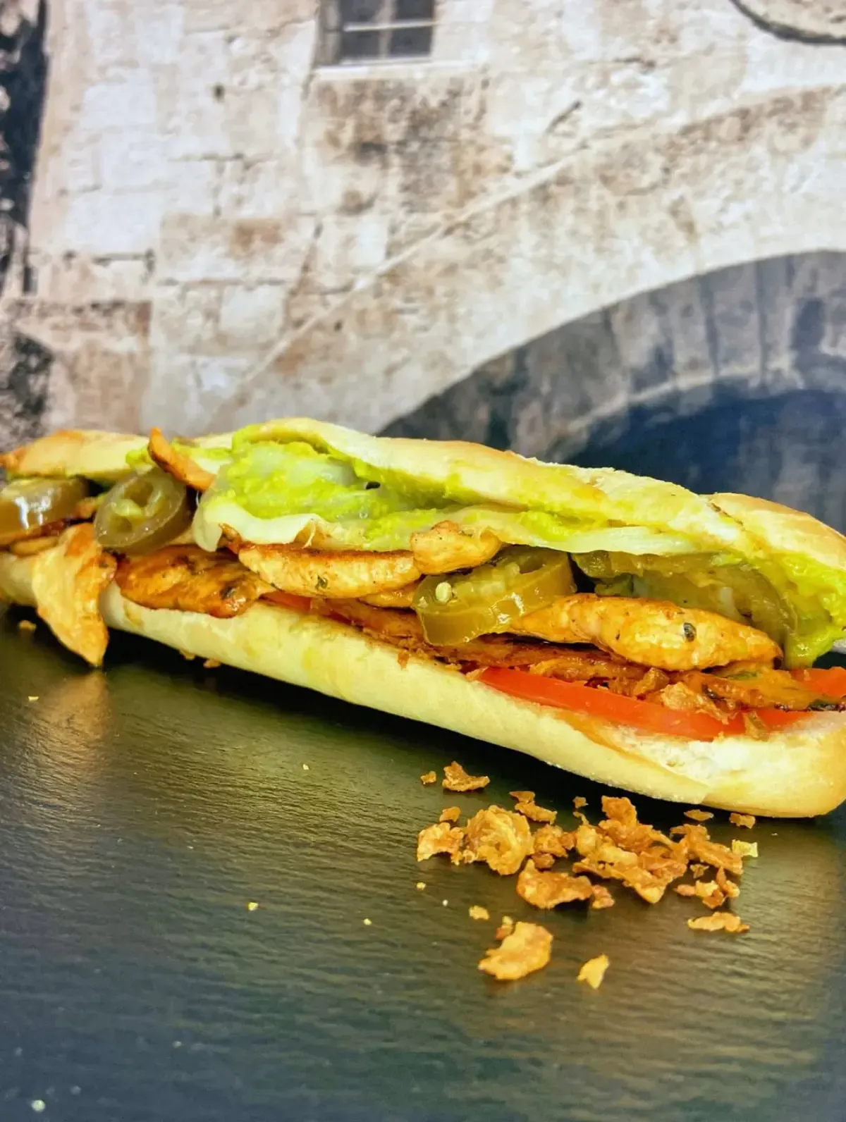 Sándwich submarino con pollo, jalapeños, lechuga y tomate, sobre una superficie negra.
