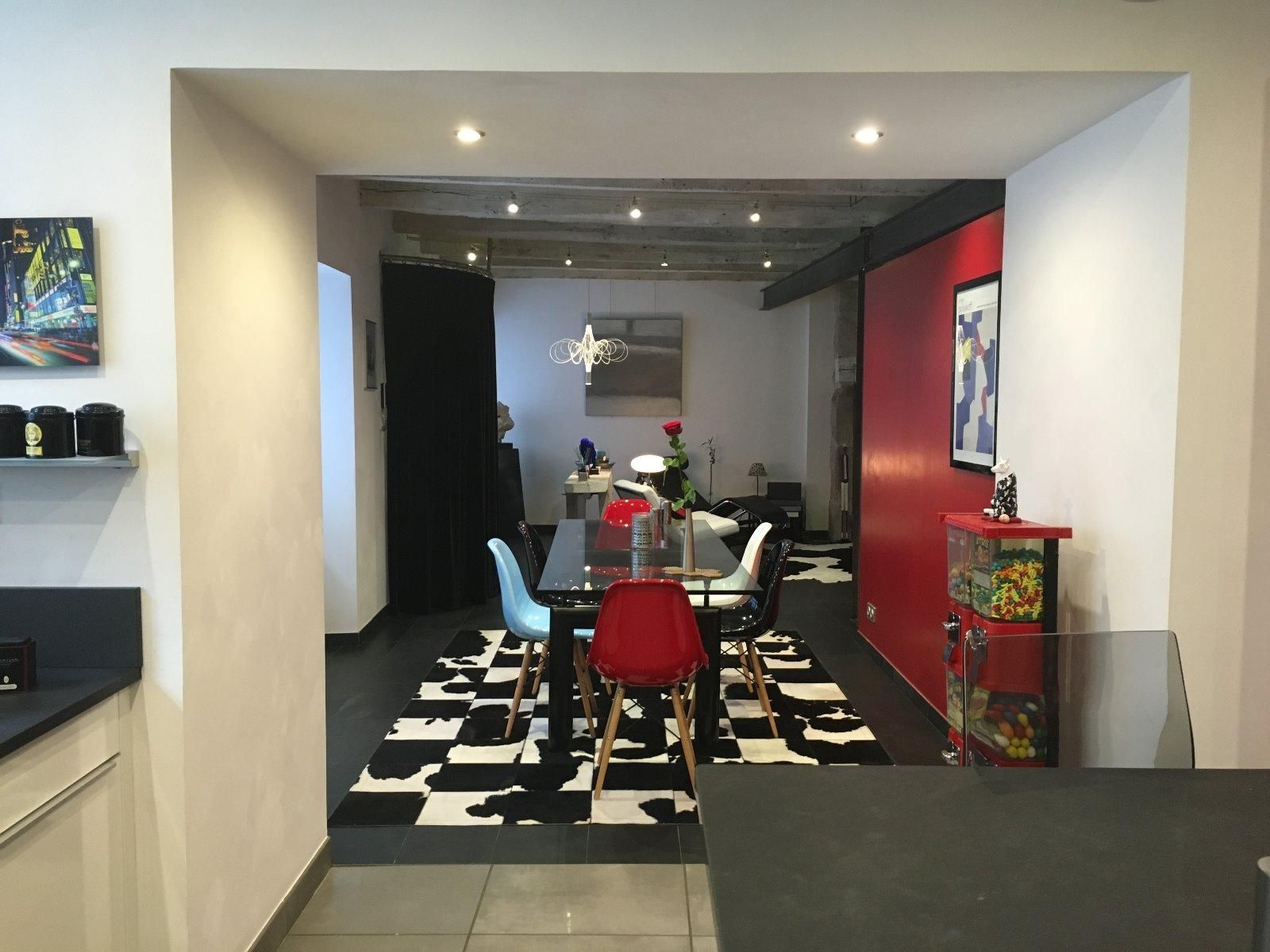 Salle à manger avec une table à manger transparente, un tapis noir et blanc et un mur rouge.