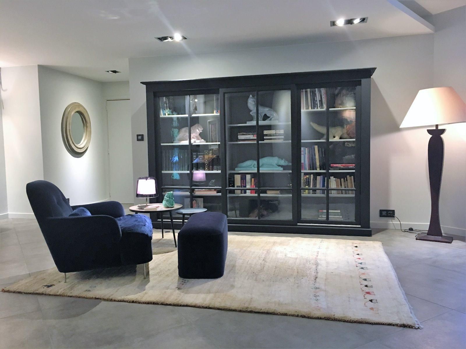 Aménagement d'un salon : tapis clair, grande bibliothèque, luminaires, fauteuils…