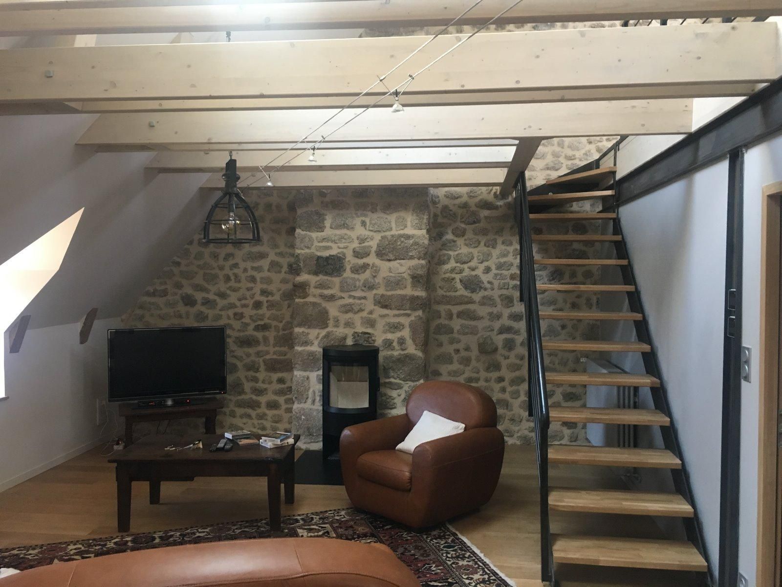 Escalier en bois présent dans un salon avec un mur en pierre