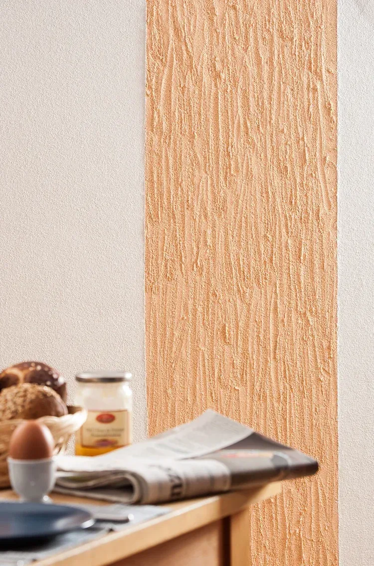 Zweifarbig verputzte Wandfläche: links hellgrau glatt, rechts rötlich-braun mit vertikaler Rillenstruktur.