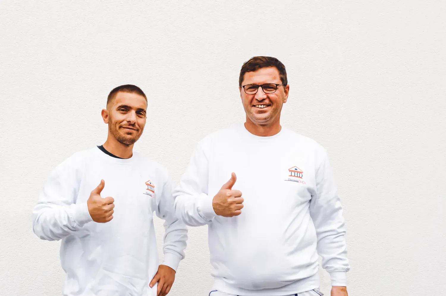 Zwei Männer in weißer Arbeitskleidung zeigen lächelnd den 