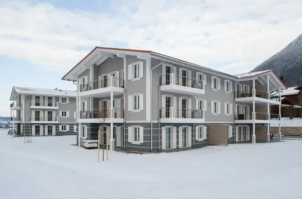 Moderne Wohnanlage mit grauer und weißer Fassade in einer verschneiten Landschaft.