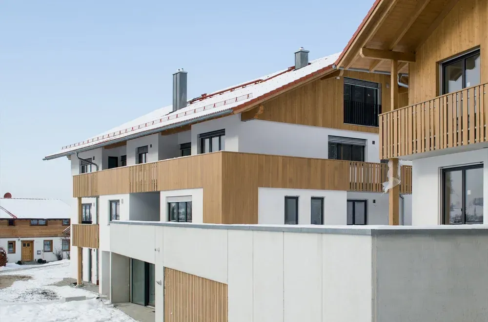 Modernes Wohngebäude mit einer Kombination aus hellem Putz und Holzverkleidung unter schneebedecktem Dach.