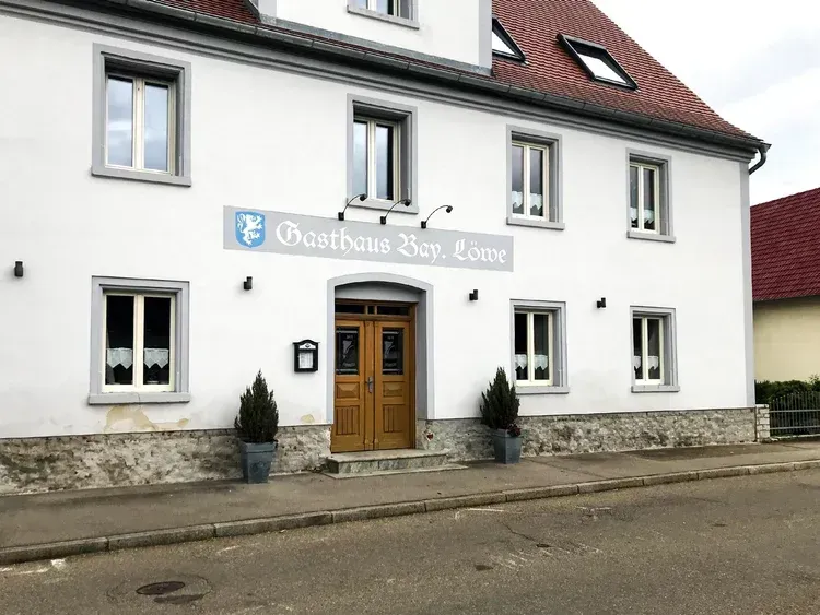 Vorderansicht eines traditionellen Gasthauses mit weißer Fassade und dunklen Fensterläden.