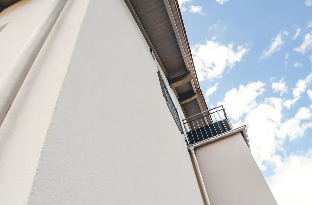 Perspektivische Ansicht einer hellen Hausfassade mit Regenrinne gegen den blauen Himmel.