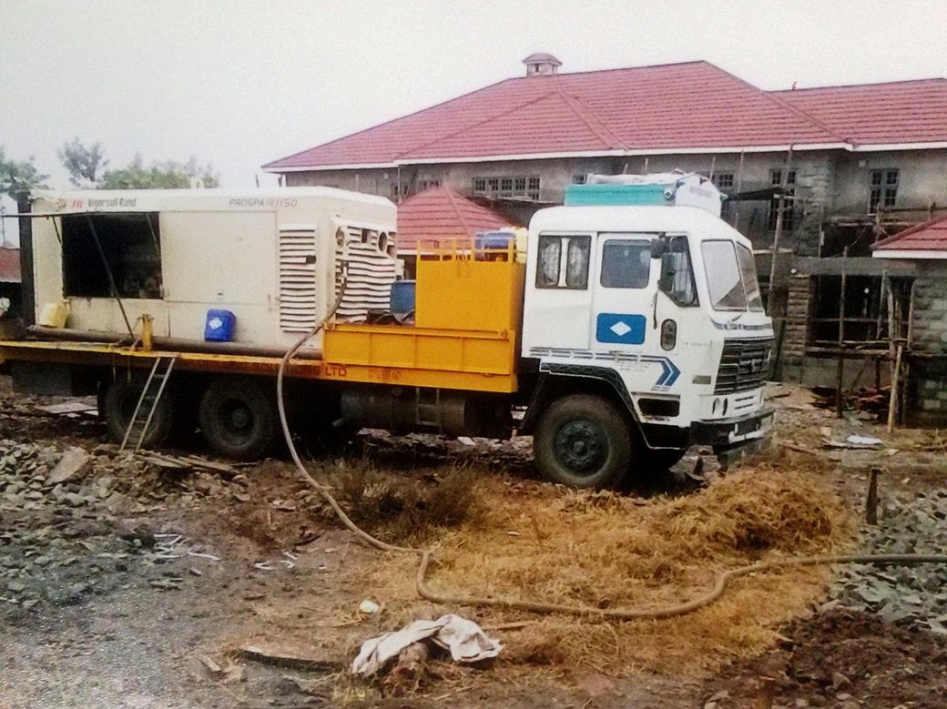 Red drilling rig in a construction site, near a pipeline, drilling into the ground.
