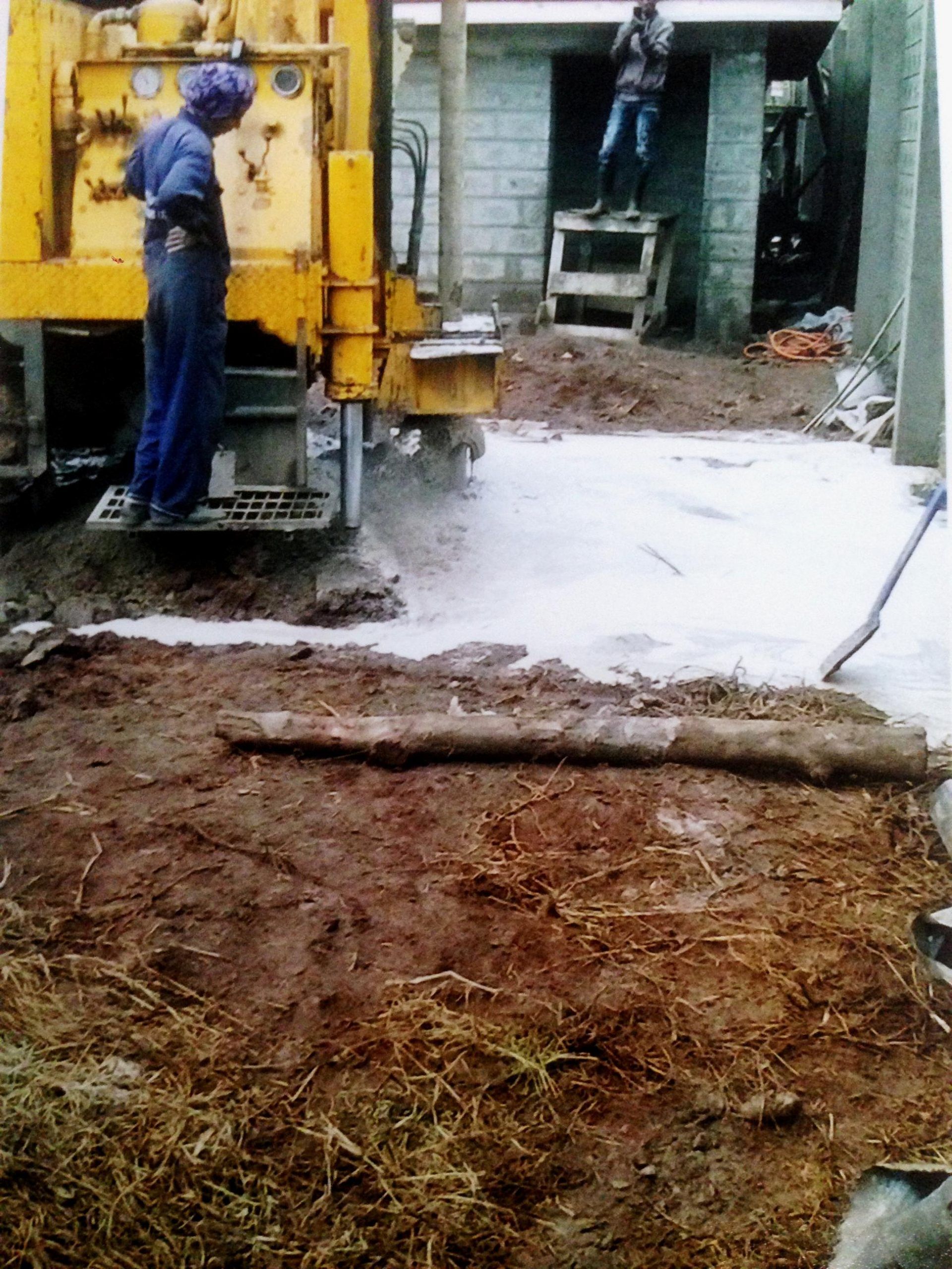 Yellow drilling machine with a worker, drilling a water well, outdoors.
