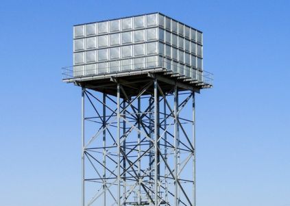 Water tower with a square tank on a metal support structure; outdoors under a blue sky.