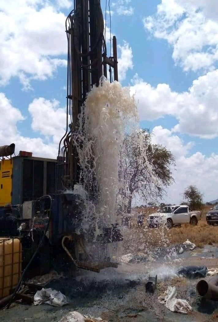 Red drilling rig in a construction site, near a pipeline, drilling into the ground.