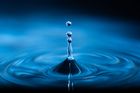 Blue water droplets falling and splashing into a pool of water, creating ripples.