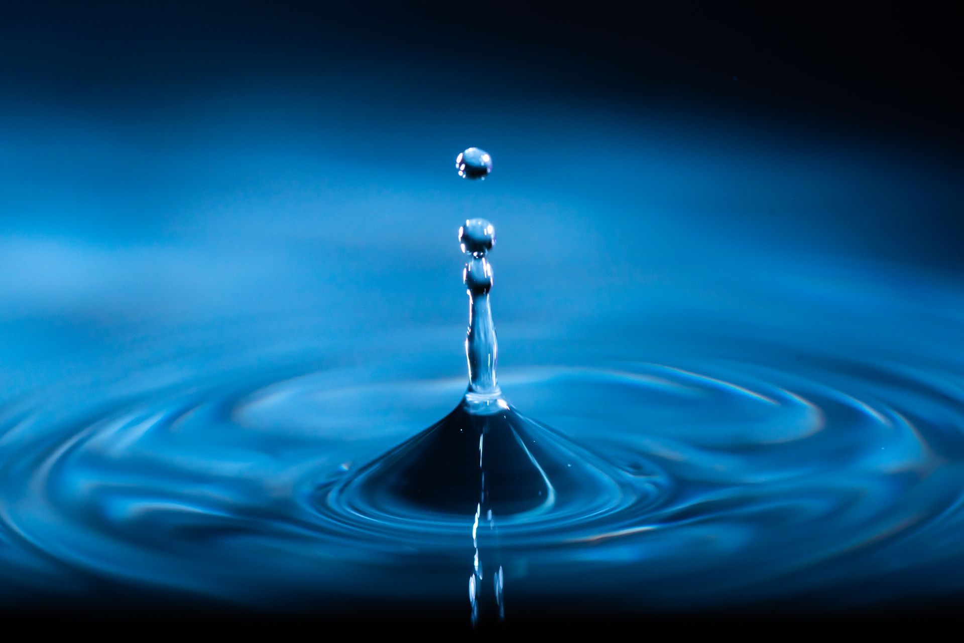 Blue water droplets falling and splashing into a pool of water, creating ripples.