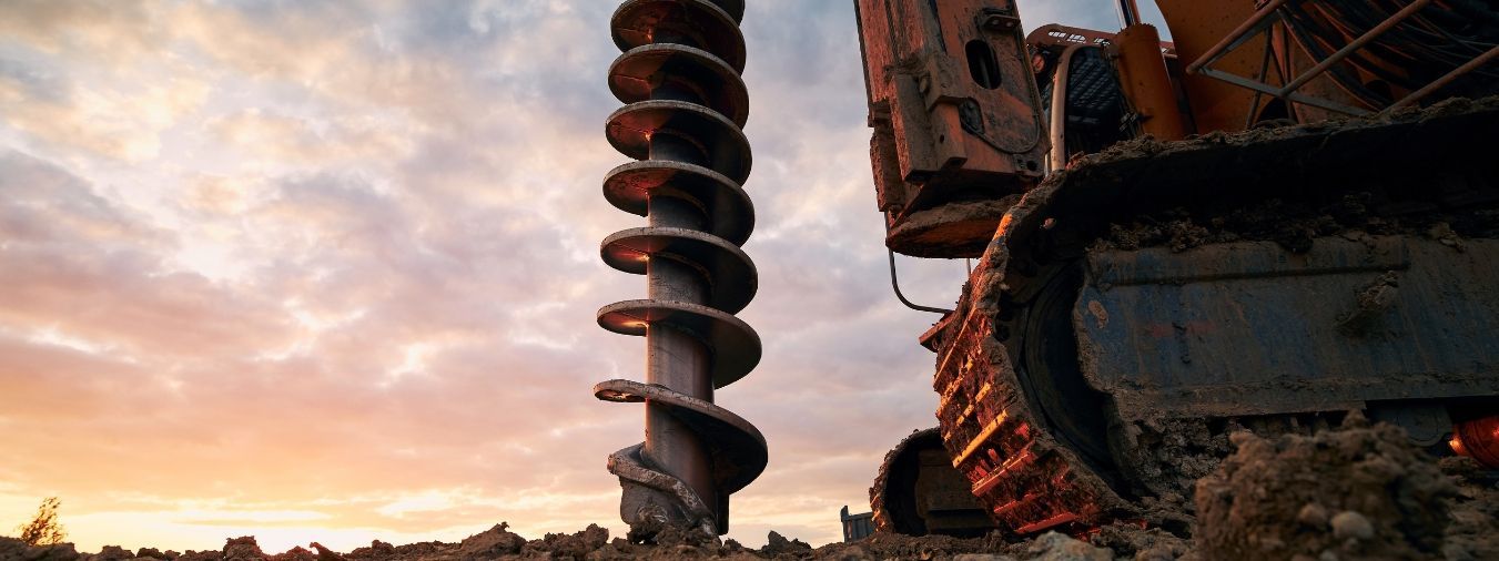 An auger drill on a construction site drills into the ground during the sunset.