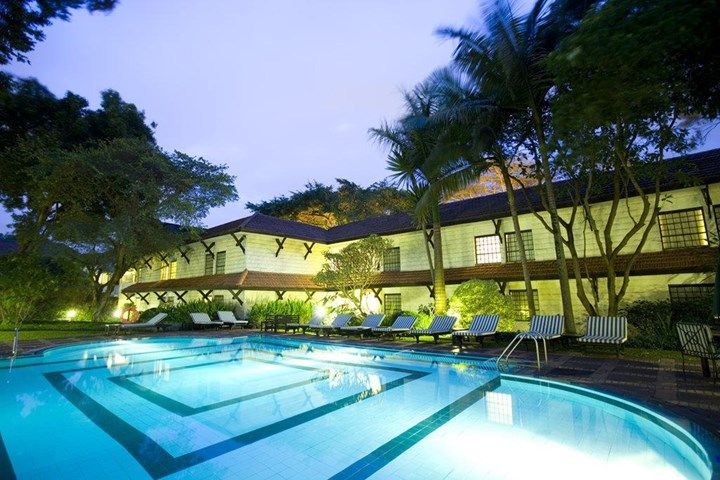 Swimming pool with geometric design, surrounded by a hotel at dusk, palm trees, lounge chairs.