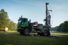 Green drilling rig on a truck in a grassy field, drilling a hole.