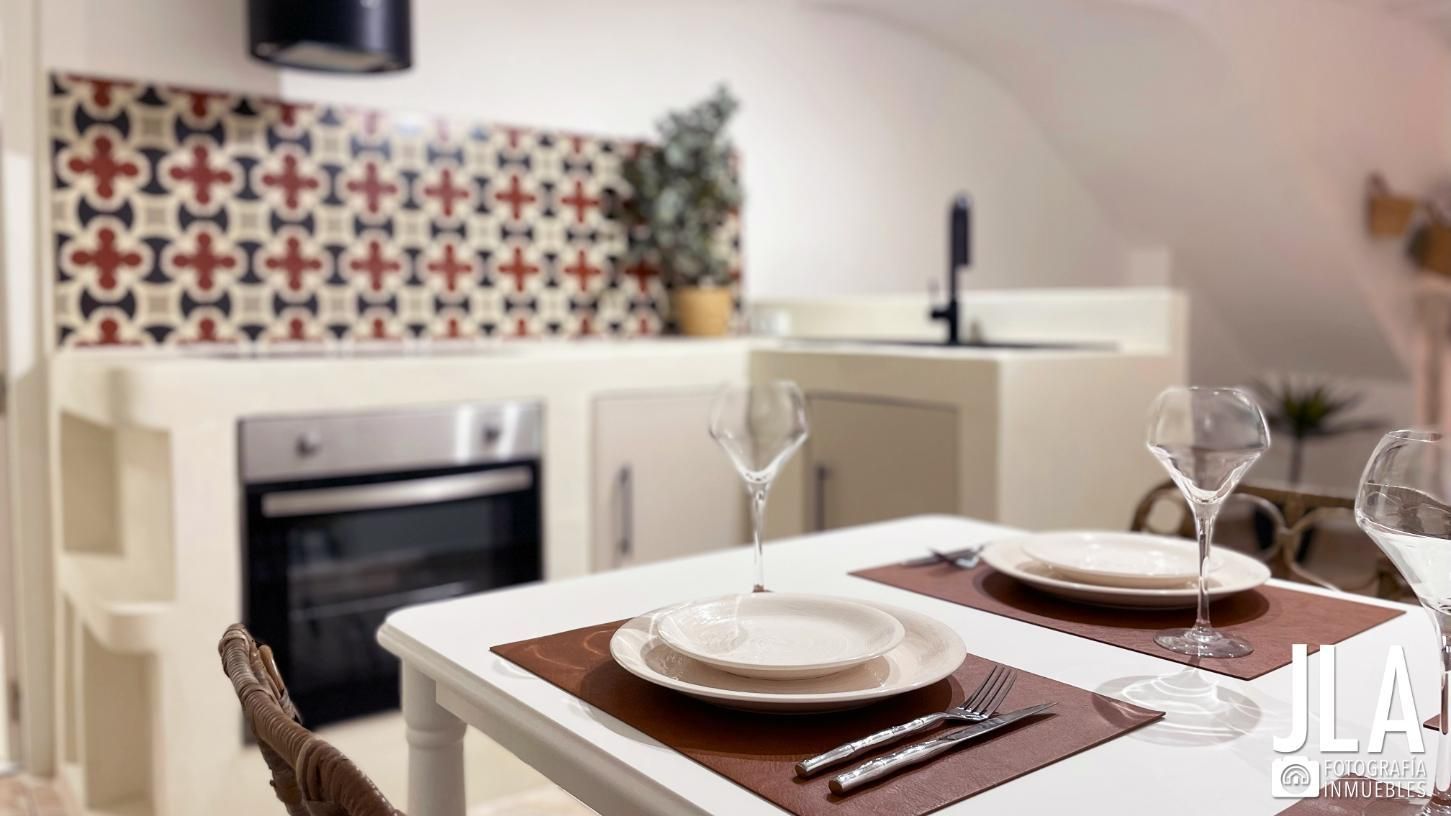 Acogedora cocina con mesa de comedor para dos. Revestimiento en rojo, blanco y marrón, gabinetes blancos y horno empotrado.