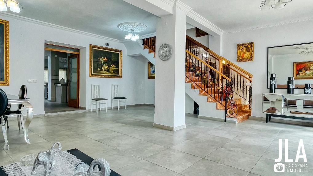 Amplia entrada con escalera, cuadros, paredes blancas y piso de baldosas.