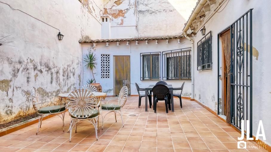 Patio con muebles de exterior, paredes blancas, baldosas de terracota y puerta de madera.