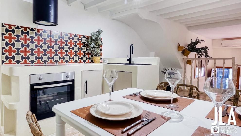 Cocina con protector contra salpicaduras estampado, gabinetes blancos, mesa de comedor con cubiertos.