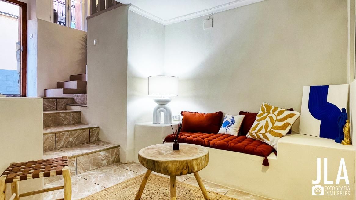 Acogedor espacio de estar con asientos incorporados, cojines rojos, mesa de madera y escaleras que conducen hacia arriba.