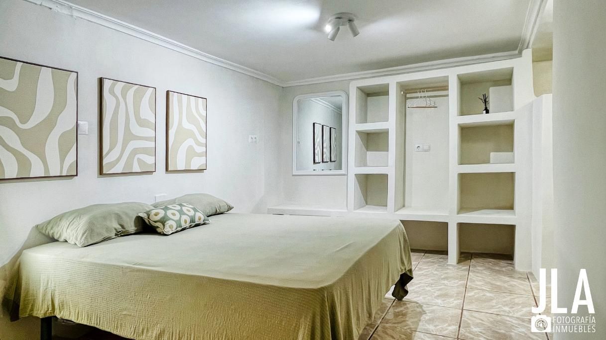 Dormitorio con cama, estanterías empotradas, obras de arte y combinación de colores neutros.