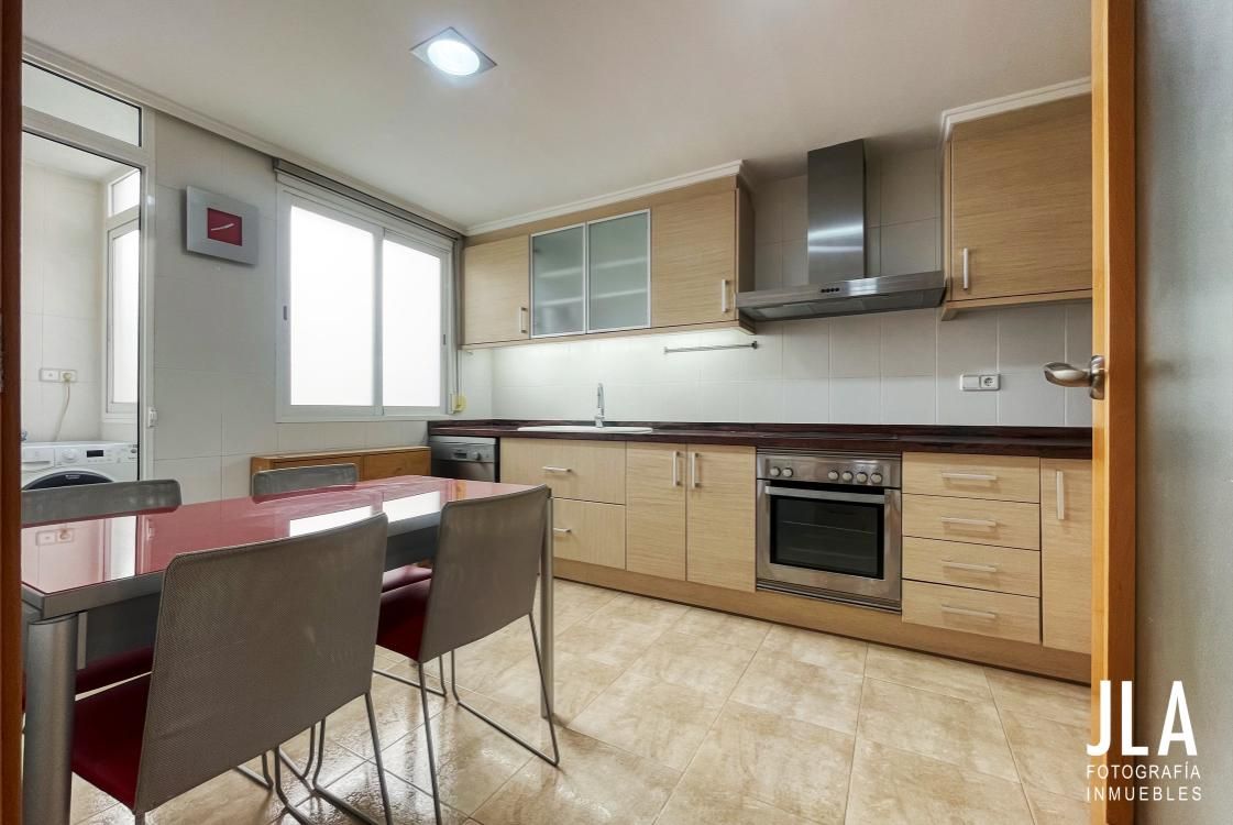 Cocina con gabinetes de madera clara, electrodomésticos de acero inoxidable y mesa de comedor.