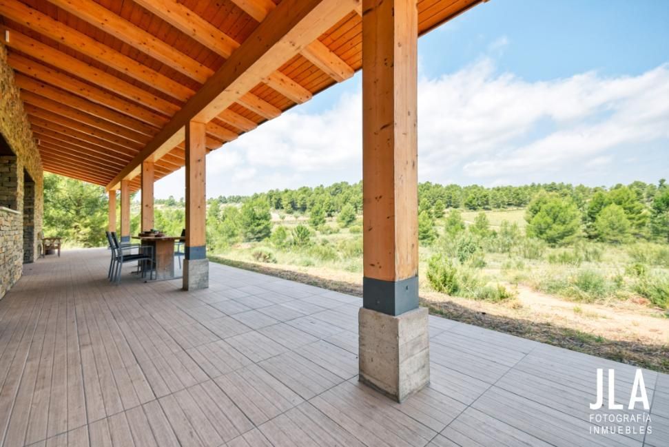 Porche cubierto con vigas de madera y pilares con vistas a un paisaje.