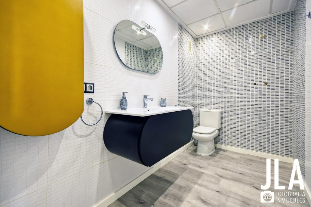 Baño moderno con tocador negro, lavabo blanco y pared decorativa estampada. 