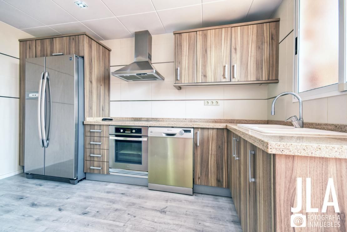 Cocina con electrodomésticos de acero inoxidable, gabinetes de madera y encimera clara.