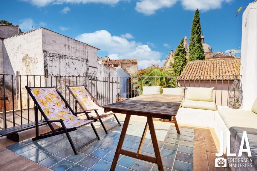 Terraza en la azotea con dos sillas plegables, una mesa de madera y un banco incorporado bajo un cielo azul.