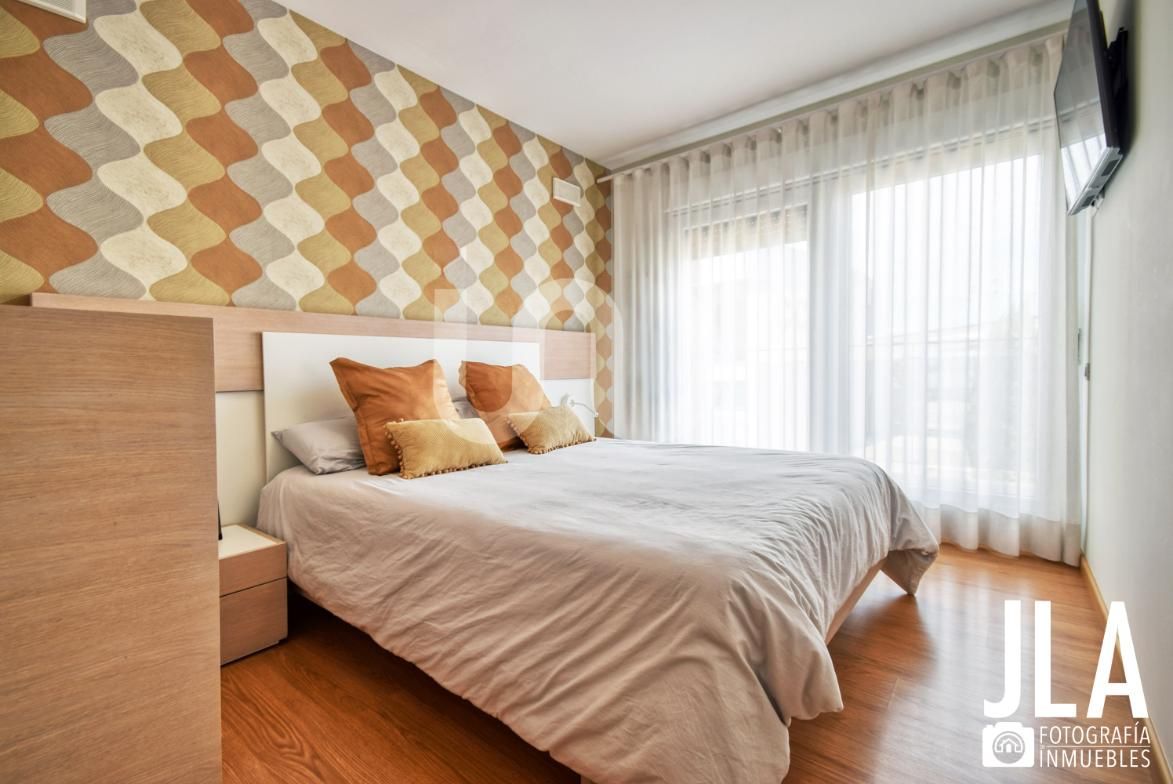 Dormitorio con papel pintado estampado, cama, mesita de noche y ventana con cortinas.