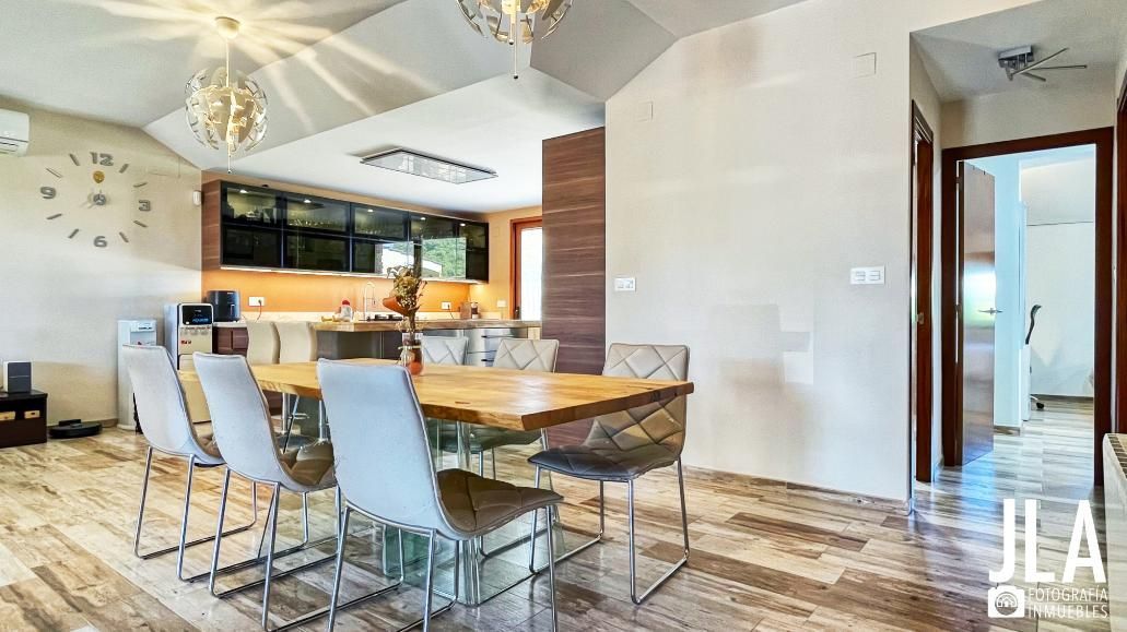 Comedor con mesa de madera, sillas y cocina al fondo.