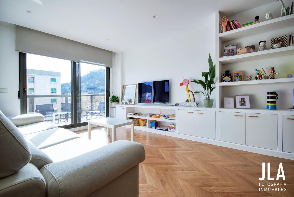 Sala de estar con sofá, TV, estanterías empotradas y un gran ventanal con vistas a un balcón.