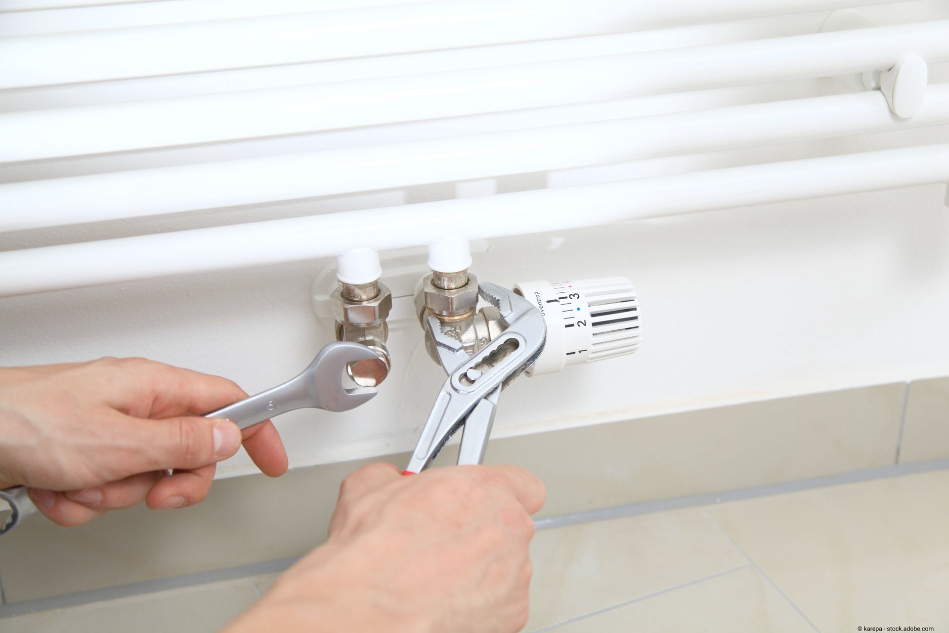 Ein Mann schraubt mit Zangen an Heizungsventilen.