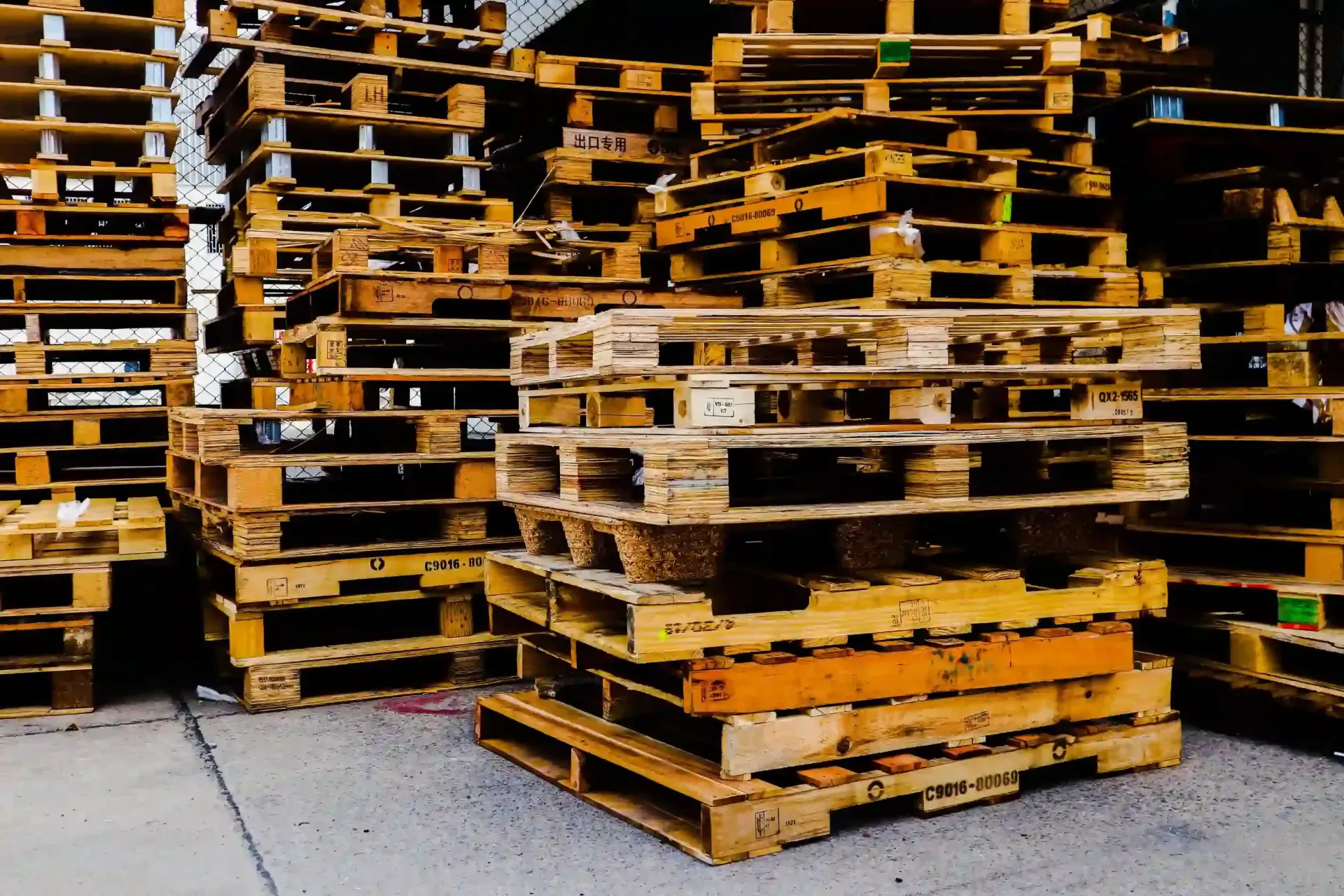 Grandes pilas de palés de madera para transporte marítimo dispuestas en el patio de un almacén al aire libre.