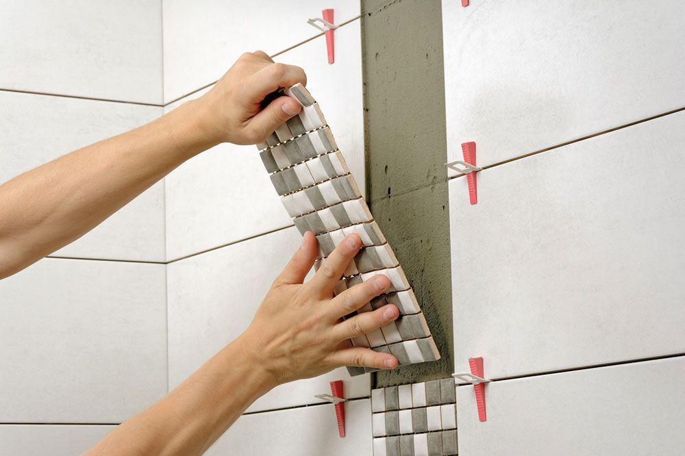 Eine Person bringt eine Fliese an einer Wand an