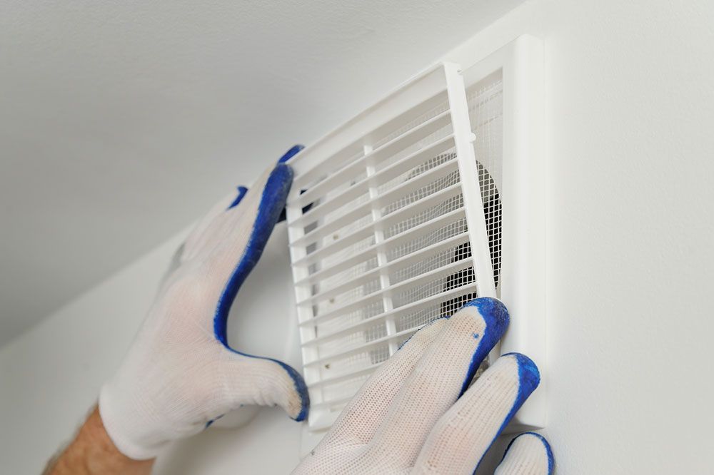 Eine Person mit blau-weißen Handschuhen installiert eine Entlüftung an einer Wand.