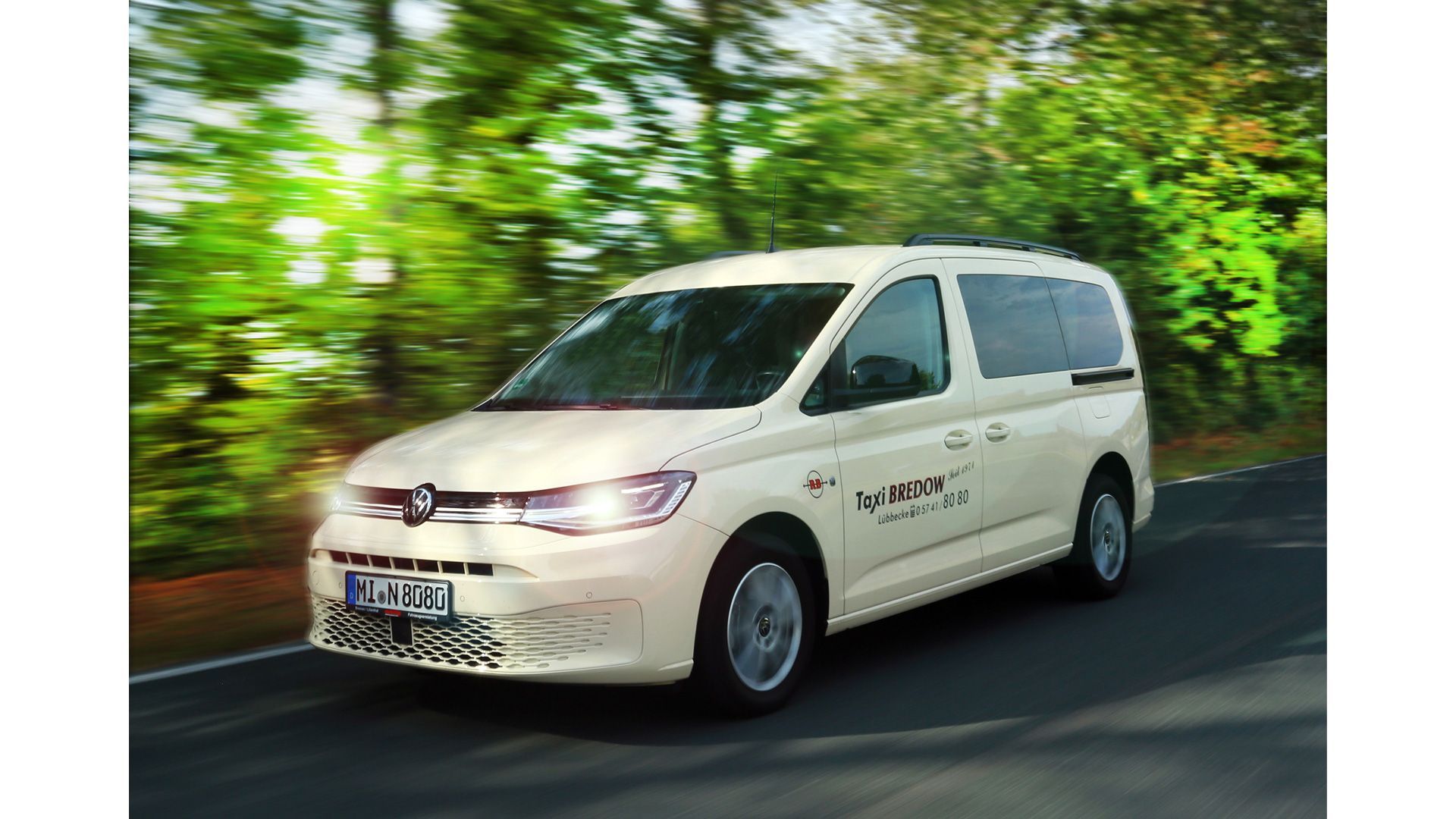 Weißer Lieferwagen mit Taxi auf der Straße, im Hintergrund verschwommene Bäume, das Auto fährt, sonniger Tag.