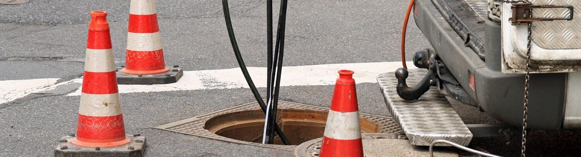 Neben einem Gullydeckel steht eine Gruppe orangefarbener und weißer Verkehrskegel.