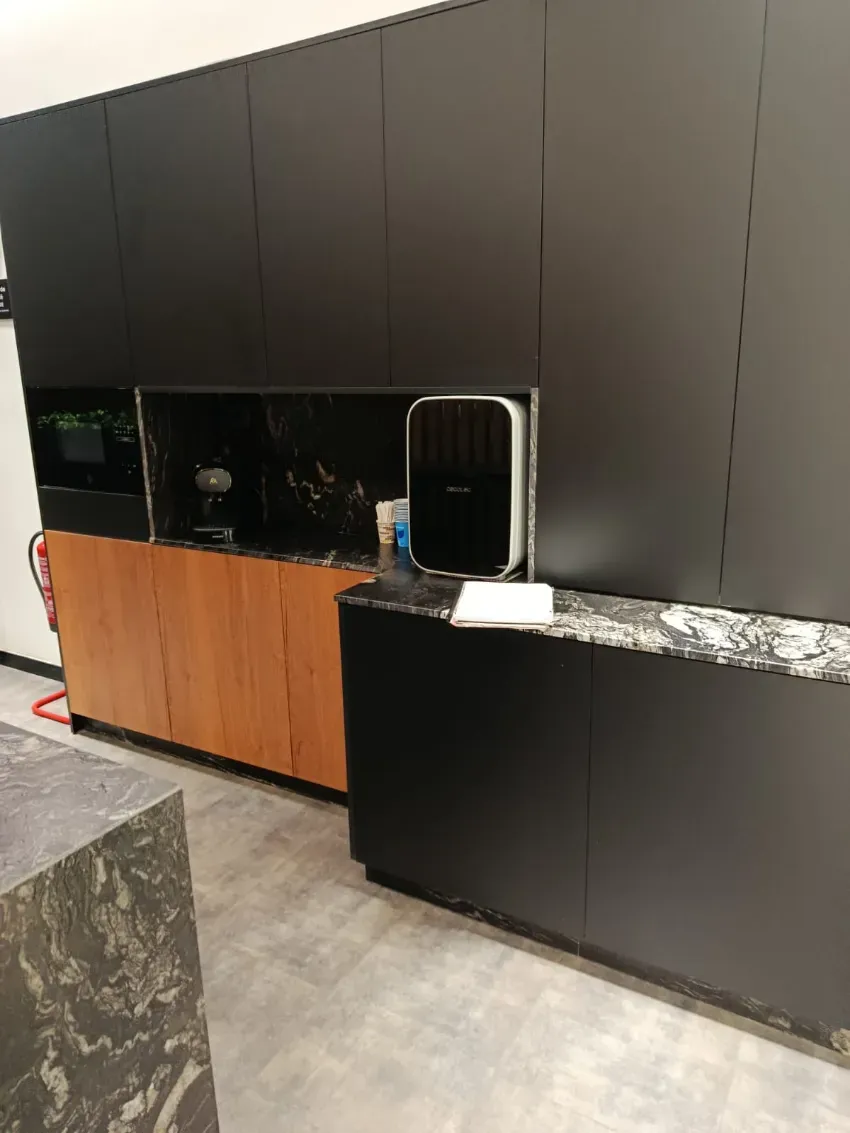 Cocina moderna con armarios oscuros, paneles inferiores de madera, encimera negra y un pequeño electrodoméstico sobre la encimera.