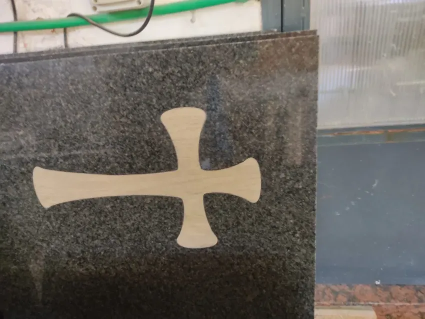 Símbolo blanco con forma de cruz en una pared de piedra oscura junto a una ventana.