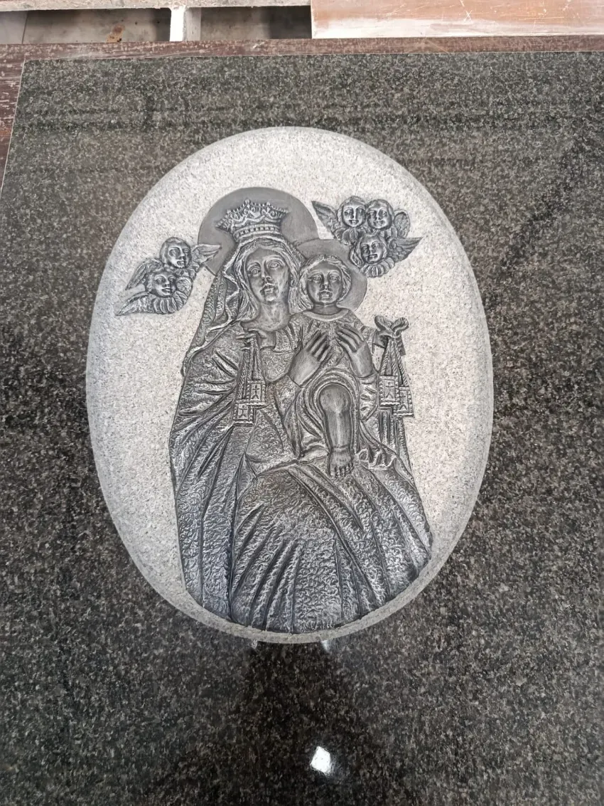 Relieve de piedra tallada que representa a un santo sentado con un niño en brazos, colocado en un medallón ovalado en una pared.
