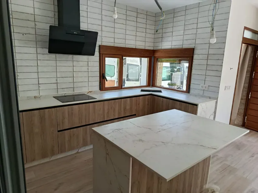 Cocina moderna con paredes de azulejos blancos, gabinetes de madera, campana extractora negra y salpicadero de mármol en la isla.