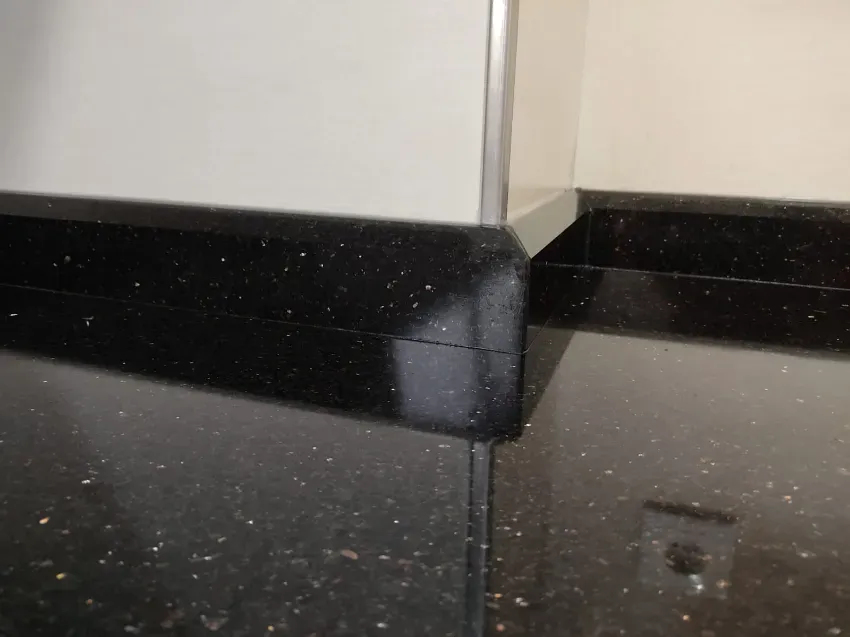 Esquina de encimera de granito negro con una pared clara y una superficie reflectante al fondo.