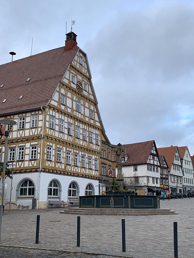 Historische Fachwerkhäuser säumen einen ruhigen Kopfsteinpflasterplatz unter einem bewölkten Himmel