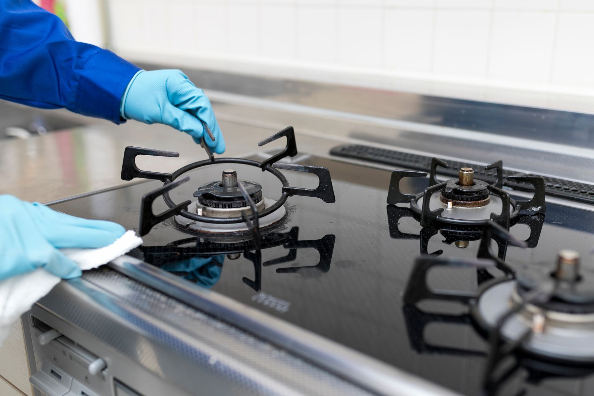 Des mains gantées nettoient une plaque de cuisson à gaz en acier inoxydable avec un chiffon.