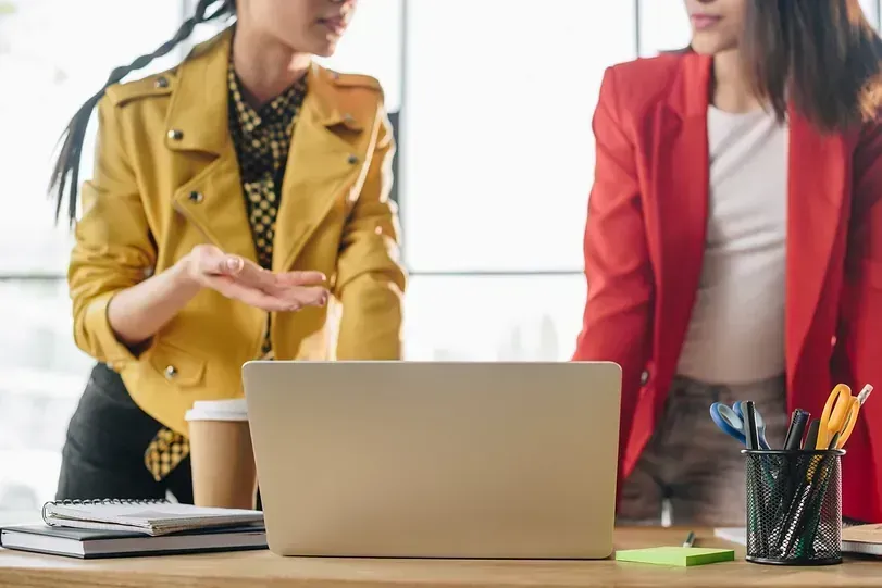 Dos mujeres están paradas una al lado de la otra frente a una computadora portátil.